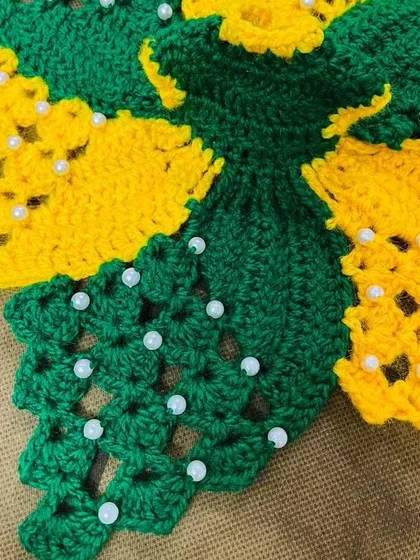 A close-up view of the detailed crochet and pearl work on the green and yellow floral dress. I carefully select each moti to complement the colors of the yarn.