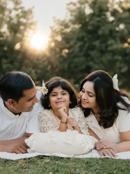 A family lies on a blanket in the grass, enjoying the sunset. This relaxed, lifestyle family portrait captures a peaceful and loving moment.