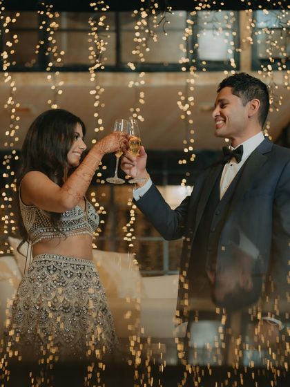 A toast to forever. The couple clinks champagne glasses, surrounded by a cascade of fairy lights, creating a magical and celebratory atmosphere for their reception.
