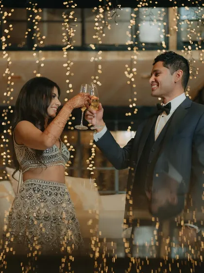 A toast to forever. The couple clinks champagne glasses, surrounded by a cascade of fairy lights, creating a magical and celebratory atmosphere for their reception.