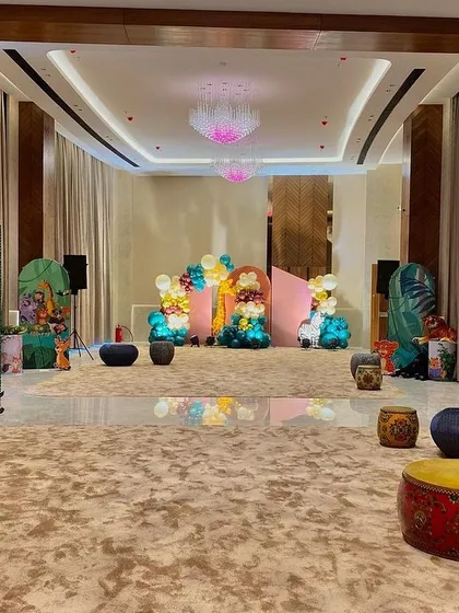 A wide view of a spacious hall decorated for a jungle theme, with green sequin walls, animal props, and low seating arrangements for a kid-friendly party.