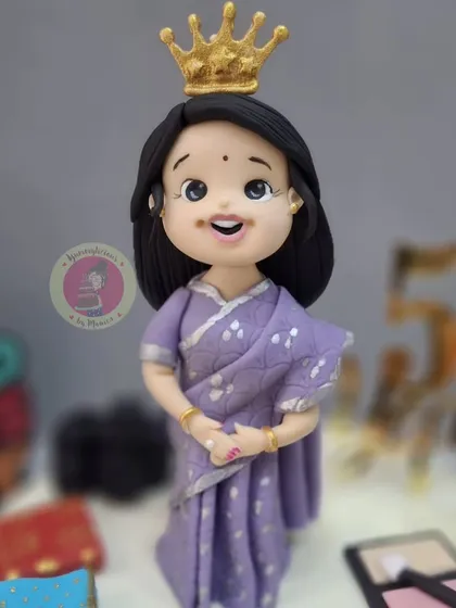 A beautiful 50th birthday cake for a mom, featuring an elegant figurine in a saree, crowned like a queen. The cake is decorated with her favorite things, like makeup and a jewelry box.