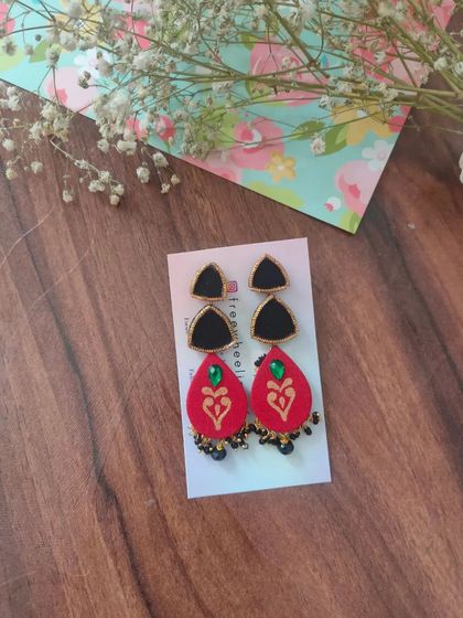 These two-part hand-painted earrings feature a black triangular stud and a red teardrop piece with a heart motif. The small black bead details add a delicate finishing touch.