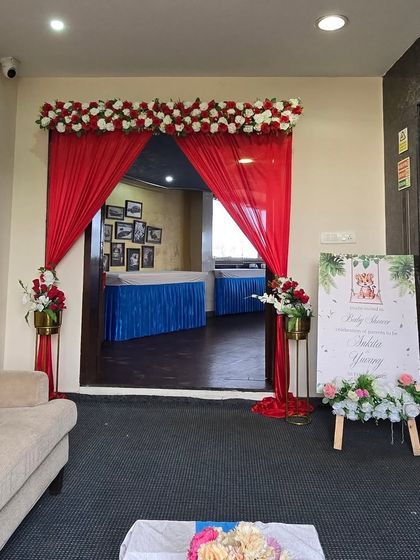 The entrance to a baby shower event, decorated with red drapes and floral arrangements.