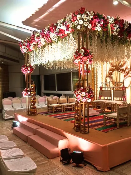 This is an example of a beautiful indoor Vidhi Mandap. The combination of a dense floral canopy with hanging white flowers and elegant gold structures creates a sacred and luxurious atmosphere within a banquet hall.