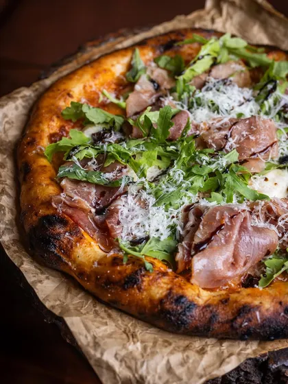 Our Prosciutto pizza is a work of art, with delicate slices of cured ham, fresh arugula, and a drizzle of balsamic glaze over a cheesy base.
