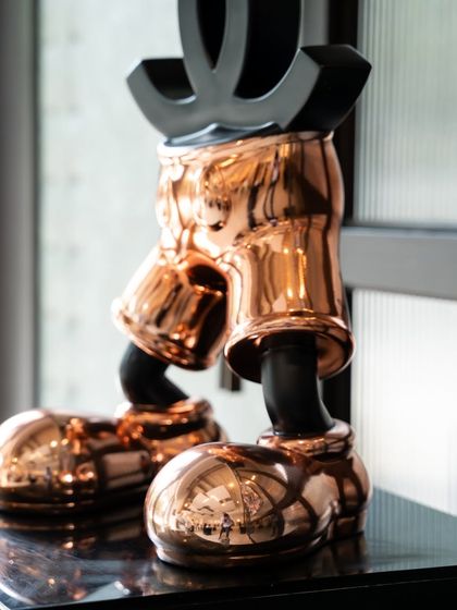 A detail shot of the "Chanel Mickey" sculpture, focusing on the rose gold chrome of its shorts and shoes.