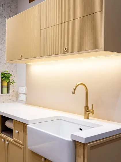 The fluted details on the upper cabinets in this kitchen add a beautiful, rhythmic texture. Paired with a farmhouse sink and brass faucet, the space feels warm, contemporary, and full of quiet character.