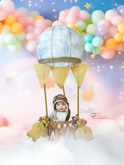 A whimsical hot air balloon setup for a sitter session, complete with a pilot cap, fluffy clouds, and a pastel balloon backdrop. This is one of my most requested creative milestone shoots.