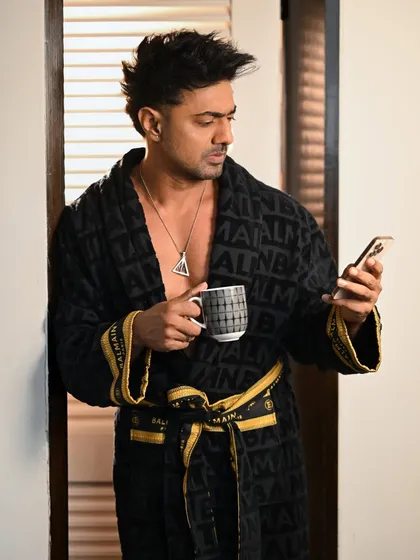 A candid moment with Dev in a bathrobe, checking his phone. This behind-the-scenes style shot feels personal and offers a glimpse into a more relaxed, off-camera persona.