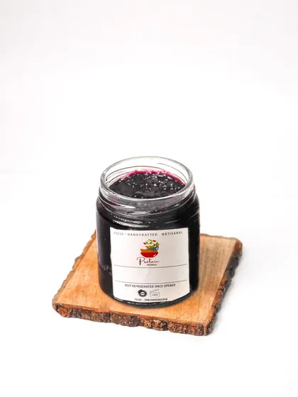 A single jar of artisanal blueberry jam on a rustic wooden coaster. This clean product shot is perfect for showcasing a brand's packaged goods.