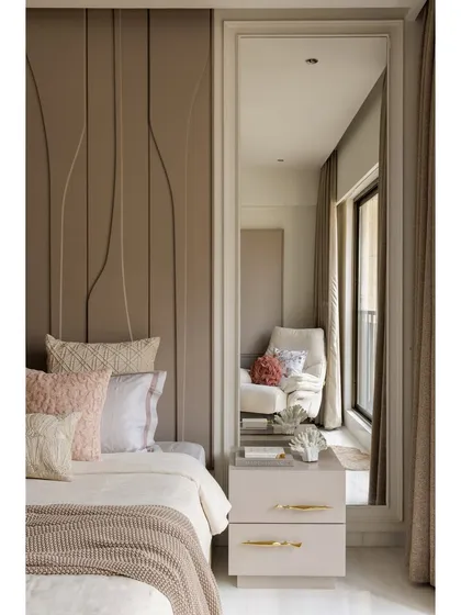 This shot highlights the details of the bedroom, including the full-length mirror that reflects the seating area and adds depth to the room. The bedside table with its clean lines and gold hardware is both stylish and functional.