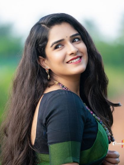 A portrait of actress Supritha Sathyanarayan, capturing her looking away with a gentle smile, set against a soft green background.