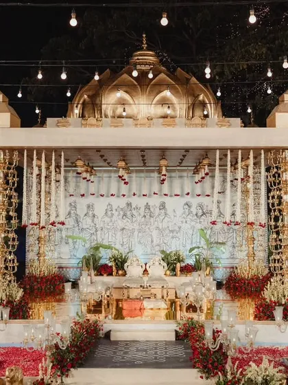 The complete view of our custom brass mandap, set in the amphitheater at night. The structure, with its 400kg pillars, domed roof, and hand-drawn backdrop, creates a stunning focal point, surrounded by red rose petals and elegant guest seating.