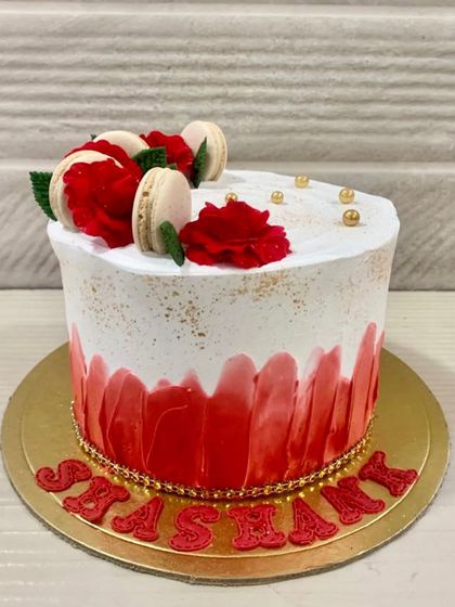 A slice of happiness with this red velvet cake, featuring a red ombre brushstroke design and topped with red sugar flowers and macarons.