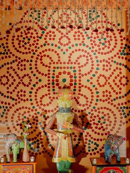 A detail shot from the Garba night decor, featuring a traditional Rajasthani figurine against a backdrop of intricate block-print patterns and a hand-dotted mandala design.