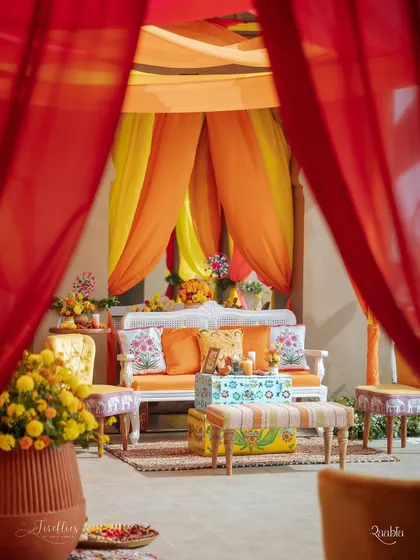 A cozy seating area draped in bright orange and yellow fabrics. The custom-printed cushions and hand-painted trunk add a personal and artistic touch to this festive corner.