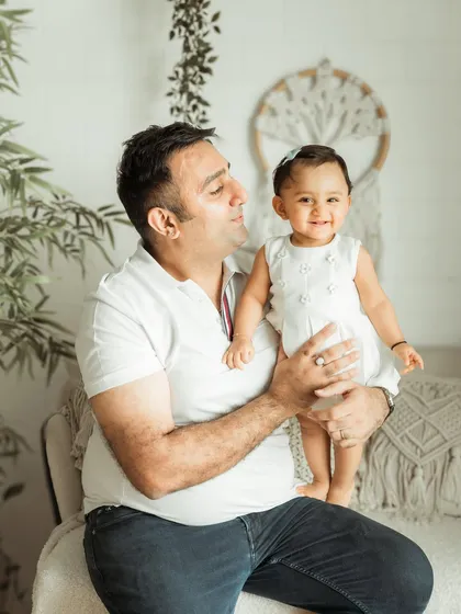 A proud father holds his smiling daughter. This studio family portrait has a clean, modern, and timeless feel.