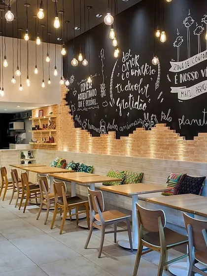 For this cafe, we created a warm, industrial-chic vibe using an exposed brick feature wall with custom chalkboard art. The space is lit with hanging Edison bulbs, and the seating arrangement with simple wooden tables and chairs provides a cozy, rustic setting for patrons.