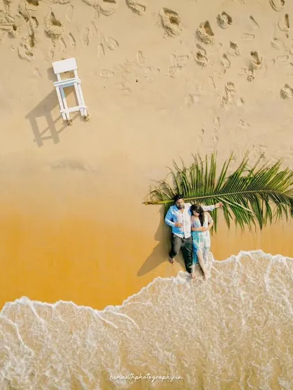 An aerial drone shot shows a couple relaxing on the golden sands of Honnavar beach, with waves gently washing ashore. This perspective adds a grand, cinematic scale to your pre-wedding album.