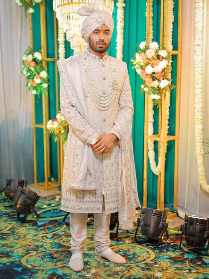 A full-length portrait of a groom in a classic off-white sherwani and turban.