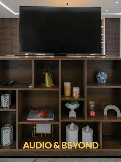 This custom-built shelving unit does more than just hold decor. It cleverly conceals a TV lift mechanism, allowing the screen to rise for viewing and retract to maintain the room's open and elegant aesthetic.