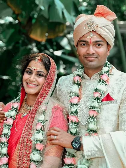 A classic portrait of a smiling couple in their wedding attire, posing together in a lush garden setting.