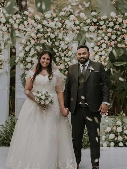 A classic wedding portrait of a couple in front of a stunning floral arch. The abundance of white flowers creates a feeling of pure elegance and romance.
