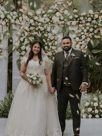 A classic wedding portrait of a couple in front of a stunning floral arch. The abundance of white flowers creates a feeling of pure elegance and romance.