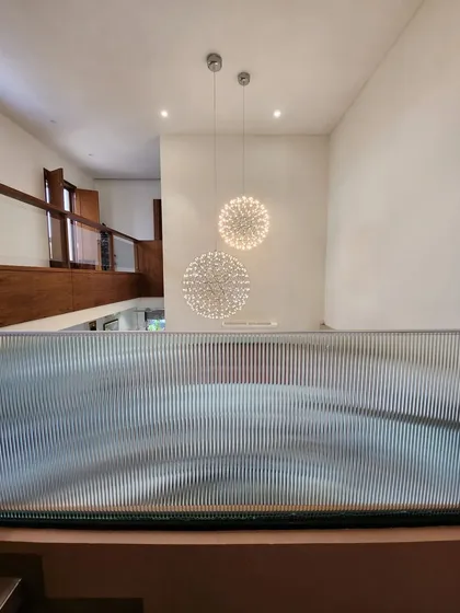Looking down from the upper level, this view captures the sculptural quality of the fluted glass railing and the cascading effect of the spherical chandeliers. This detail shows how we play with texture and light to connect different floors.