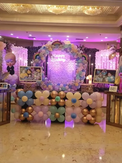 A full view of a Boss Baby and Frozen combined theme party in a banquet hall. The setup includes a central ring backdrop, character stands, and themed photo displays.