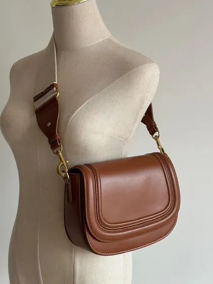 A full view of the brown Noble bag on a mannequin. This demonstrates the length of the fabric strap and how the bag looks as part of an outfit.