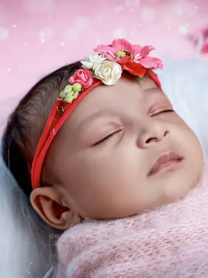 A close-up of the baby's face from the pink session, showing her floral headband and a tiny pink teddy bear.