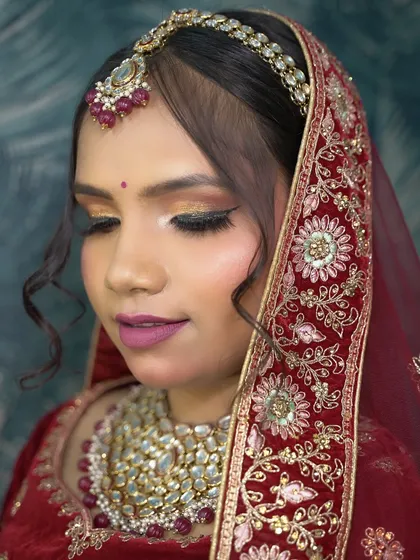 A photo of a glamorous bridal look with a red velvet lehenga and shimmery eye makeup, taught in a previous batch.