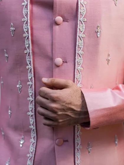 A close-up on the delicate hand-embroidery and button details of the pink Indo-Western jacket, showcasing the high level of craftsmanship.