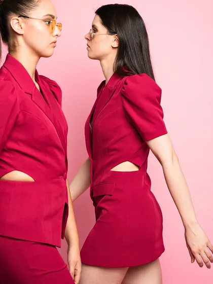 A closer crop of the two models in magenta, emphasizing the confident attitude and sharp tailoring of the garments. The face-to-face pose creates a strong visual tension.