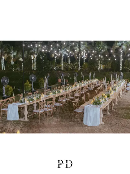 The full setup for an elegant outdoor reception dinner. The long, parallel tables create a sense of community, while the string lights and palm trees add a touch of tropical romance.