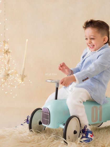 A candid moment of pure glee from a little boy playing on his toy car. His laughter is the highlight of this fun portrait.