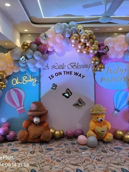 A cute baby shower setup combining teddy bears and a hot air balloon theme. The pastel and gold balloon arch frames the backdrop which reads 'A Little Blessing is on the Way'.