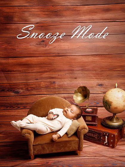 Explorer in training, currently recharging. This adorable newborn is fast asleep on a tiny couch in a vintage-themed setup with a globe and gramophone, dreaming of future adventures.