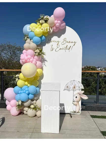 A whimsical 'Every Bunny is Excited' baby shower backdrop. This rooftop setup features a pastel balloon garland and a cute bunny prop, perfect for a springtime celebration.