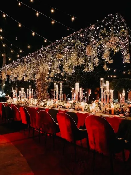 We designed this long dining table for an intimate yet grand dinner. A canopy of fairy lights and hanging florals above the table, paired with rich red velvet chairs, created a warm and dramatic dining experience.