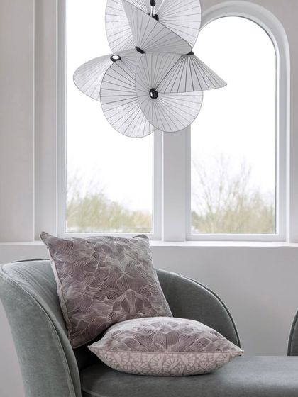 A close-up of the Serpentine Light, showing its delicate, fan-like paper structure against a window, emphasizing its translucency and lightness.