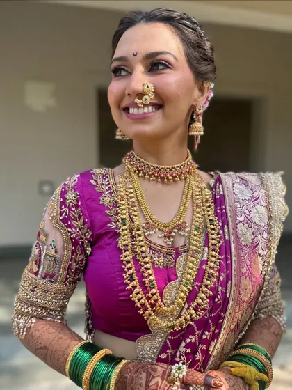 A close-up portrait of the bride, her face lit up with a beautiful smile. The focus is on the stunning traditional jewelry and the flawless makeup application.