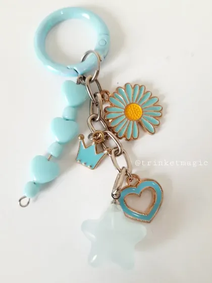 A detailed look at the pastel blue charm keychain. It features a daisy, a crown, a heart, and a star, all in a beautiful blue and white color palette.