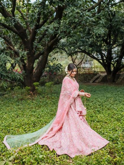 A bride in a flowing pink and green lehenga, walking through a lush garden, a picture of grace and happiness.
