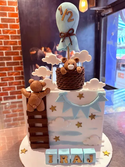 A "half birthday" cake with a hot air balloon theme, featuring a cute teddy bear floating among the clouds.