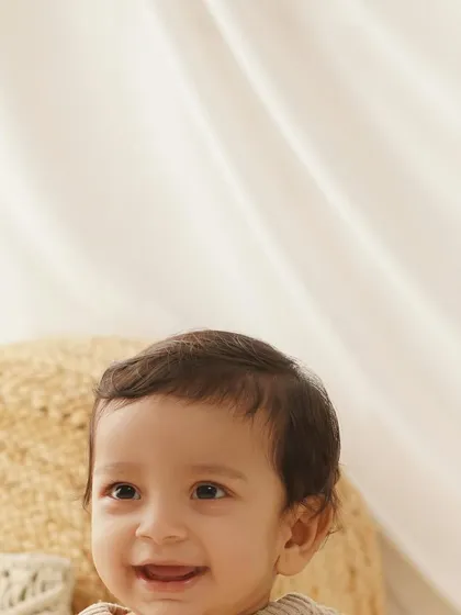 Capturing the bright, happy smile of a slightly older baby. This simple, light-filled setup with natural textures like a jute pouf keeps the focus on his joyful expression.