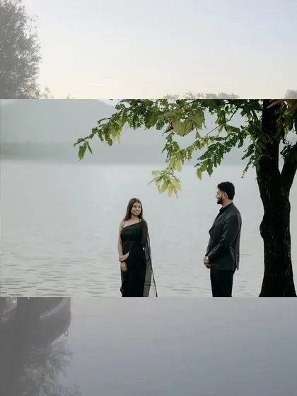 A moody and atmospheric shot of a couple by the lake, framed by trees and a misty background.