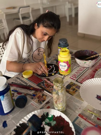 A participant carefully applies dots of paint to her coaster, enjoying the relaxing and creative process of dot painting.